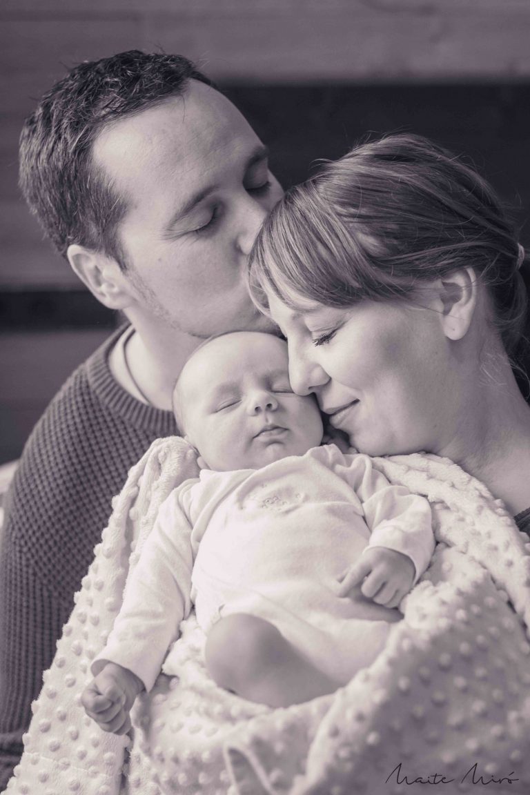 Fotografía newborn en su hogar arropado por su madre mientras su padre le da un beso