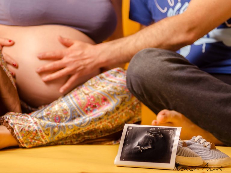 Muestra de una ecografía y de fondo la mano de un padre acariciando la barriga de la futura madre